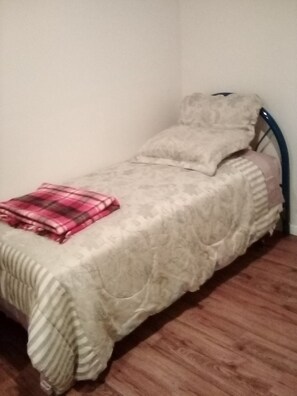 Cozy retreat with a single bed, featuring a light-colored bedspread and a simple metal bed frame.