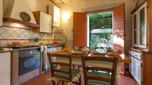 A kitchen with a brick oven, wooden chairs, and a view of greenery outside. - Cilamino by Interhome (Peccioli)