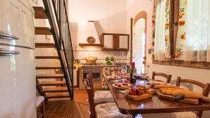Una cocina con una mesa de comedor dispuesta para cuatro personas, un refrigerador y una escalera que sube a otro nivel.