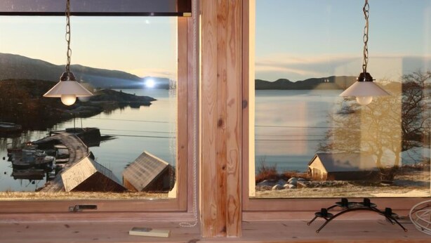 A room with a large window overlooking a lake, two hanging lamps, and a wooden floor. - Bakkafall by Interhome (Førde)