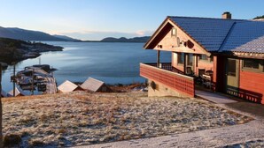 A house with a balcony overlooking a lake, a dock with boats, and a mountainous backdrop. - Bakkafall by Interhome (Førde)