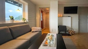 A modern living room with a sofa, a coffee table with decorative items, a fireplace, and a television mounted on the wall. - Bakkafall by Interhome (Førde)