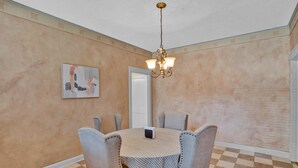 A dining area with a round table, six chairs, a chandelier, a painting, and a door. - Cozy On Creswell (Shreveport)