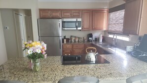 Uma cozinha moderna com bancadas de granito, eletrodomésticos de aço inoxidável, armários de madeira e uma ilha central com uma chaleira.