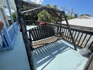 Eine Holzterrasse mit einer Bank, umgeben von einem weißen Zaun und Palmen.
