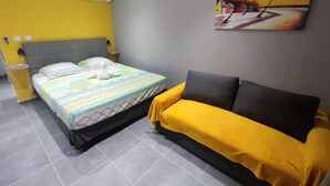 A hotel room with a bed, a sofa, and a painting of a beach scene. - Gray Diamond Studio (Le Diamant)