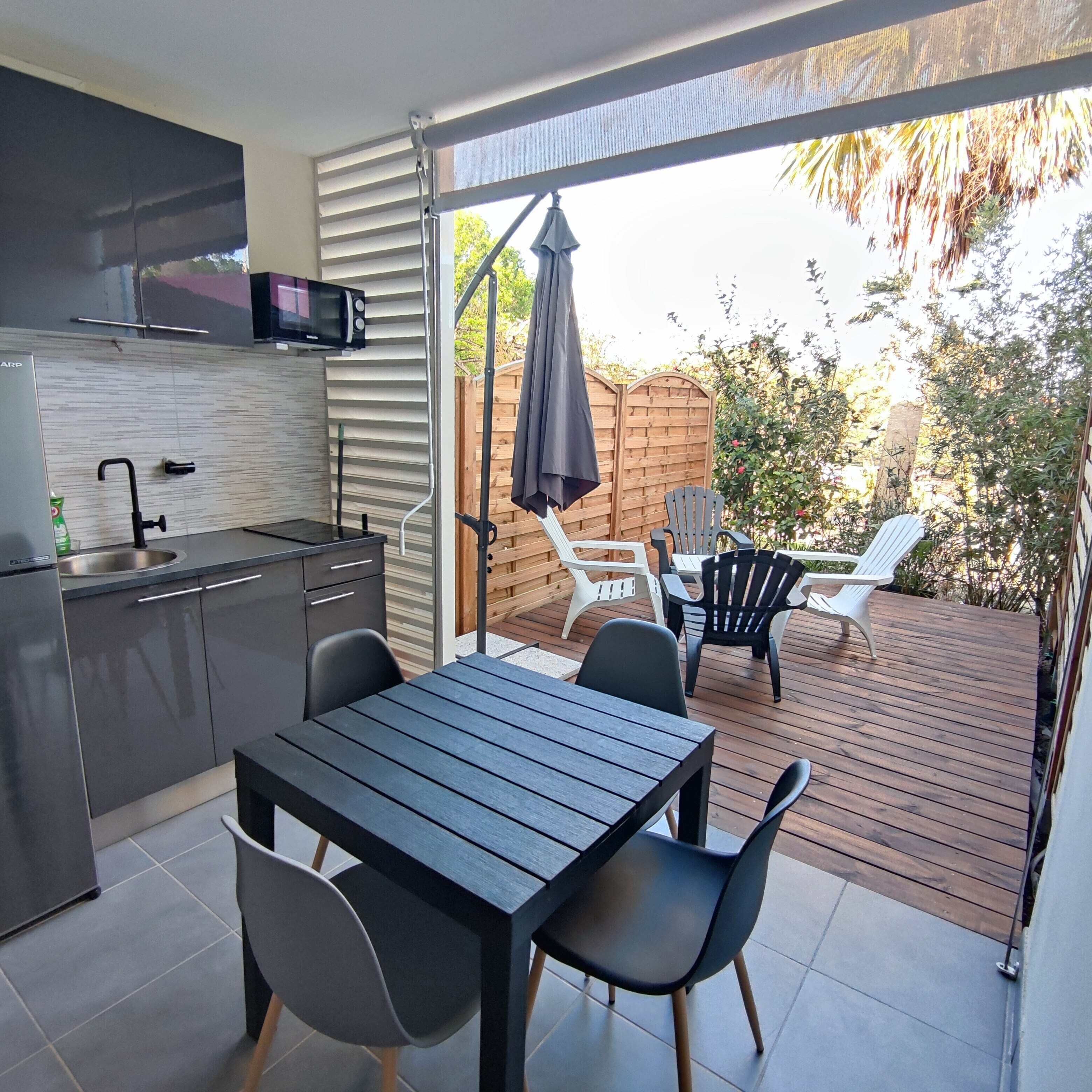 A modern kitchen with a microwave, sink, and cabinets, leading to an outdoor patio with a table, chairs, and a wooden deck.
