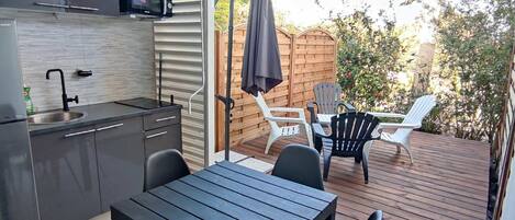 A modern kitchen with a microwave, sink, and cabinets, leading to an outdoor patio with a table, chairs, and a wooden deck.