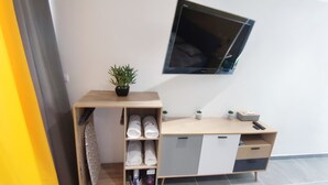 A modern room with a wooden desk, a mounted TV, a potted plant, and a shoe rack. - Gray Diamond Studio (Le Diamant)