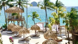A beach resort with thatched umbrellas, lounge chairs, and a wooden structure overlooking the ocean. - Gray Diamond Studio (Le Diamant)