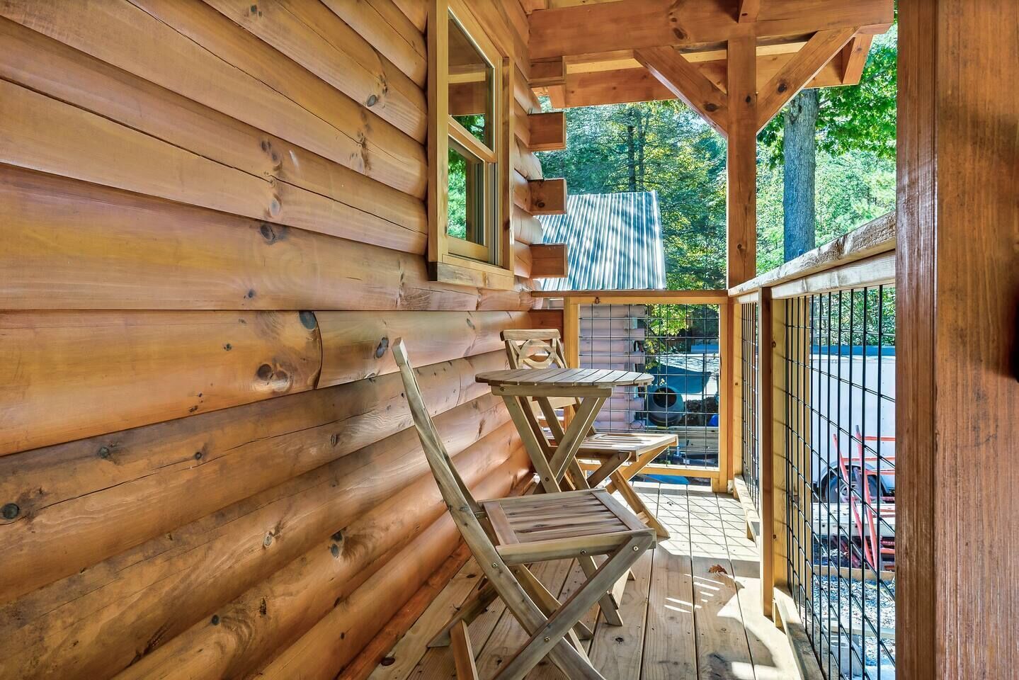 A wooden cabin with a porch, a metal gate, and a view of the surrounding forest.