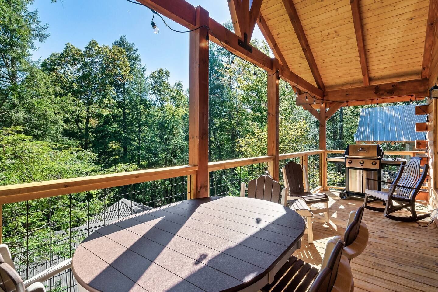 A wooden deck with a table and chairs, a grill, and a view of a forest.