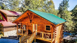Eine Blockhütte mit grüner Dachdeckung, einer Holzterrasse und einer Treppe zum Eingang.
