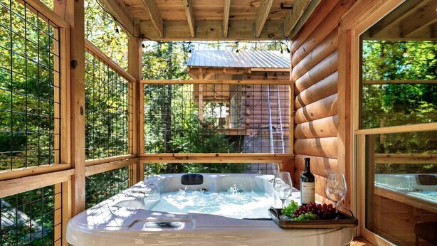 Eine Holzhütte mit Whirlpool, einer Weinflasche und einem Glas auf der Terrasse.