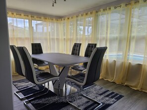A dining area with a round table and six chairs, a patterned rug, and a window with yellow curtains.