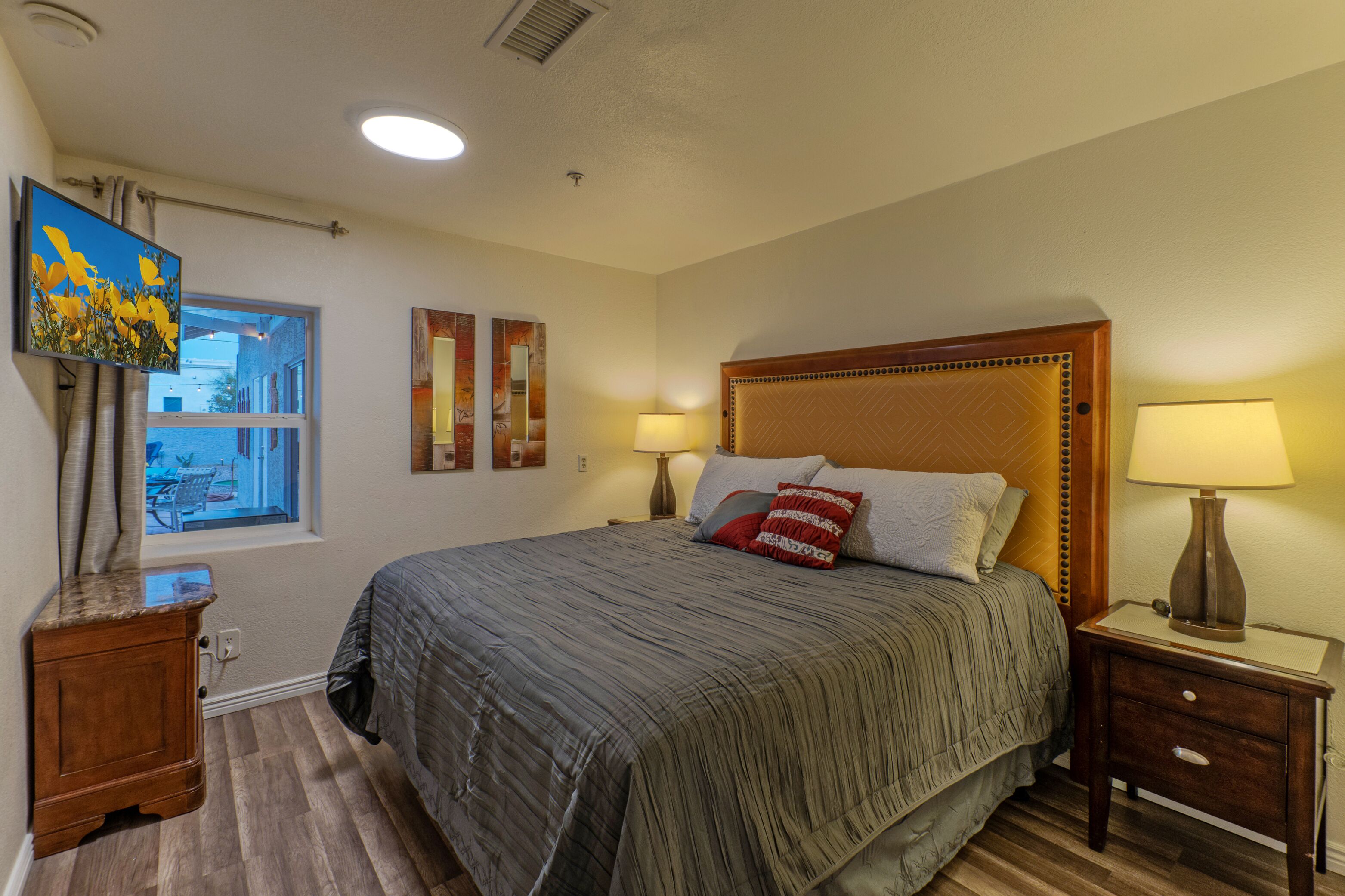 A neatly arranged bedroom with a large bed, two bedside lamps, a wooden nightstand, a window with curtains, and a painting on the wall.