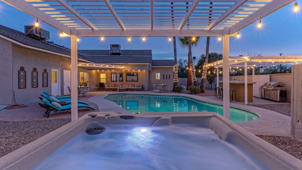 A backyard with a hot tub, pool, and outdoor seating area under a pergola with string lights. - ADA Access, One Story, Htd POOL, Spa, Putting Green, Games, Fire Pit, TVs All BRs (Scottsdale)