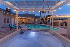 A backyard with a hot tub, pool, and outdoor seating area under a pergola with string lights. - ADA Access, One Story, Htd POOL, Spa, Putting Green, Games, Fire Pit, TVs All BRs (Scottsdale)