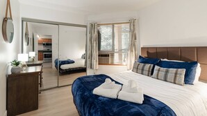 A bedroom with a bed, bedside table, mirror, and a view of a kitchen and balcony. - Amazing Family Retreat with PRIVATE hot tub! Steps to the Village and slopes (Whistler)