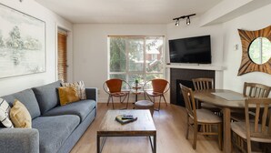 A living room with a sofa, coffee table, TV, fireplace, and dining area. - Amazing Family Retreat with PRIVATE hot tub! Steps to the Village and slopes (Whistler)