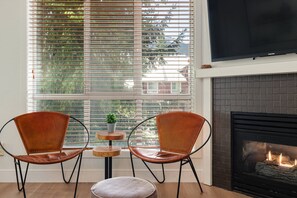 Une pièce avec une cheminée, deux fauteuils en cuir, une petite table avec une plante et un téléviseur fixé au mur.