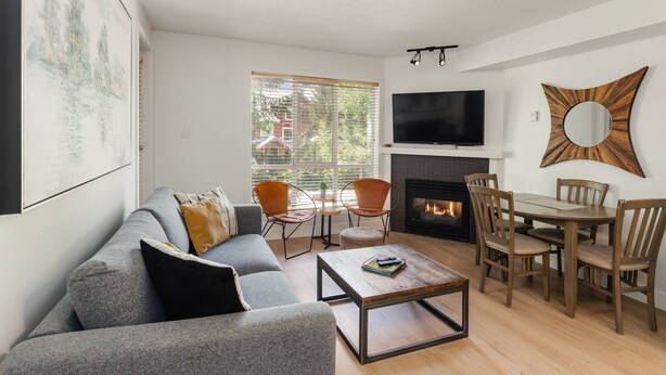 A living room with a sofa, coffee table, TV, fireplace, and dining area. - Amazing Family Retreat with PRIVATE hot tub! Steps to the Village and slopes (Whistler)