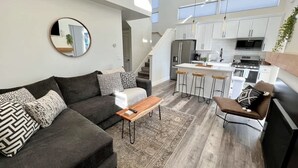 Un salon moderne avec un canapé, une table basse et un coin repas équipé de tabourets de bar.