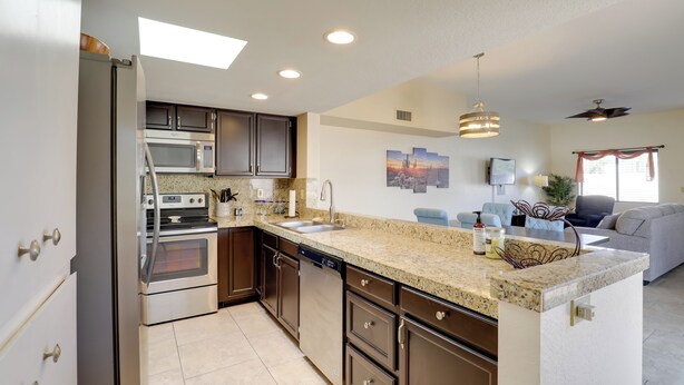 A modern kitchen with stainless steel appliances, granite countertops, and a dining area with a gray sofa and a ceiling fan. - Sunny Tucson Townhome w/ Patio & Mountain Views! (Tucson)