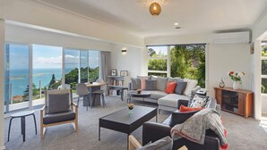 Amplia sala de estar con un ventanal que ofrece una vista panorámica, un rincón acogedor con sofá y sillones, una pequeña mesa de comedor y una estantería.