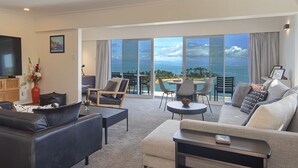 Un amplio salón con un sofá grande, una mesa de centro y un televisor. Cuenta con un balcón con vistas al mar.