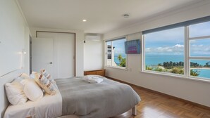 Un dormitorio con una cama grande, suelo de madera, ventana con vista al mar y una puerta.