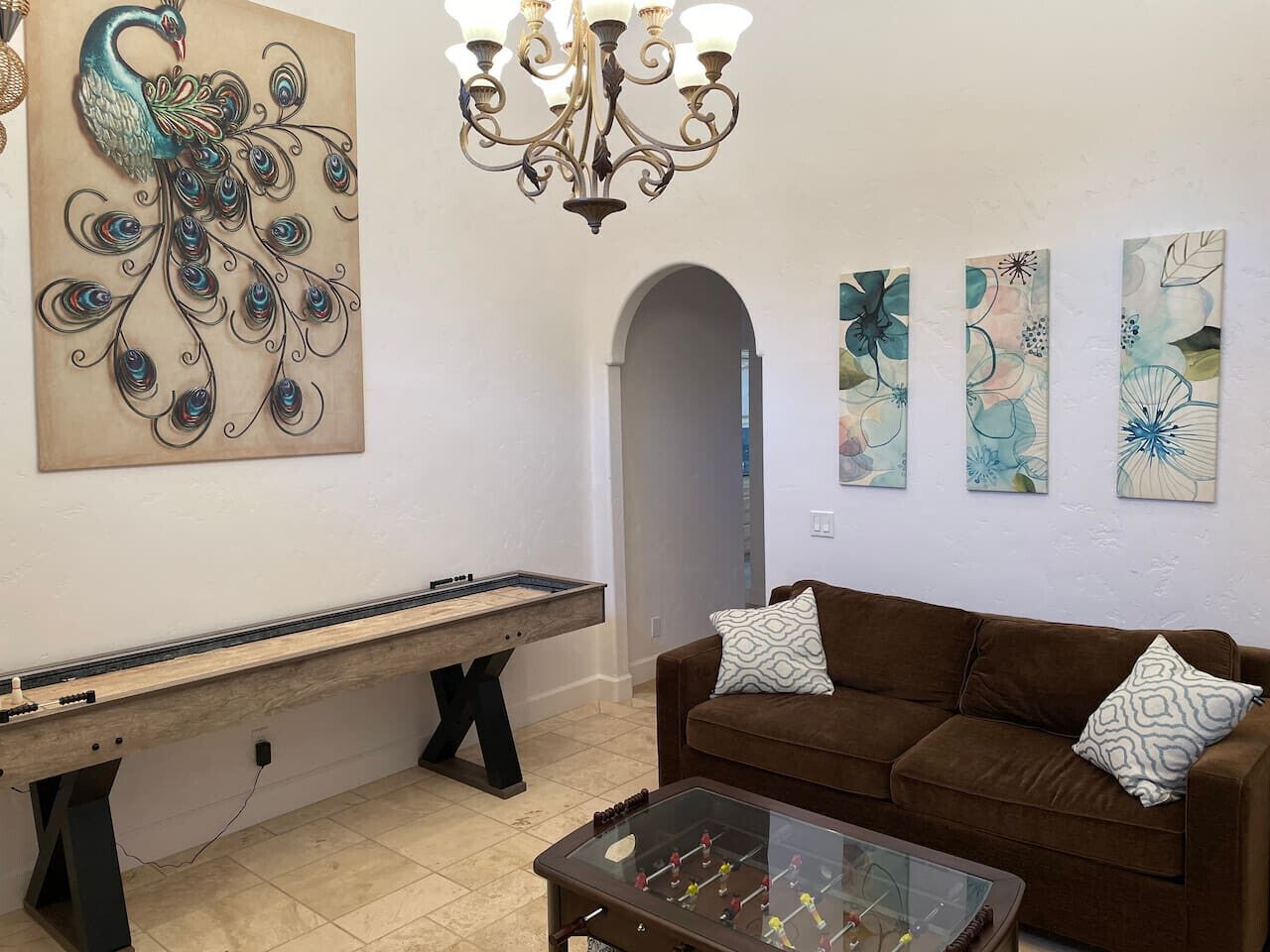 A living room with a pool table, a brown sofa, and three wall-mounted paintings.