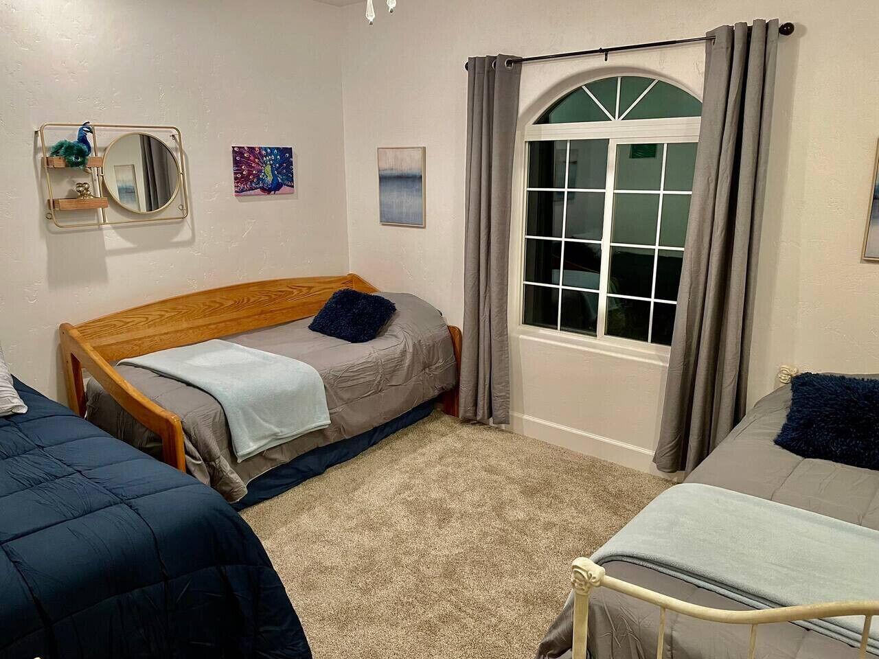 A bedroom with two beds, a window with curtains, a mirror, and artwork on the walls.