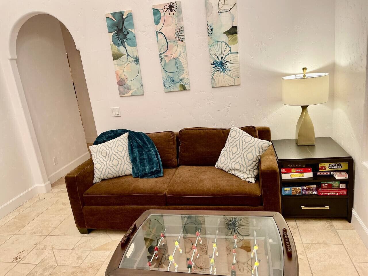 A living room with a brown sofa, decorative pillows, a glass coffee table, and a lamp on a side table.
