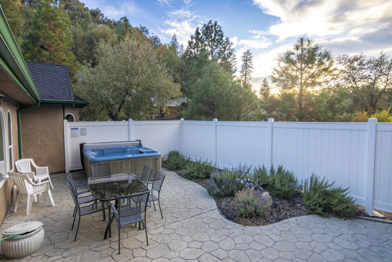 Un patio al aire libre con un jacuzzi, una zona de estar y una cerca blanca.