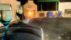 Un área de hidromasaje con chimenea, dos sillas azules y dos copas de vino.