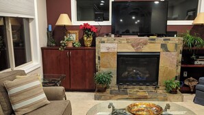 A living room with a stone fireplace, a sofa, a glass coffee table, and a television mounted above the fireplace.