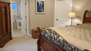 A bedroom with a large bed, a dresser, a nightstand, and a door leading to another room.
