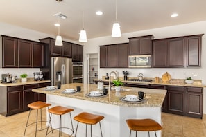 A modern kitchen with dark wood cabinets, stainless steel appliances, a large island with bar stools, and pendant lighting.