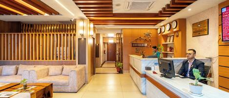 A hotel reception area with a wooden reception desk, a sofa, and a reception counter.