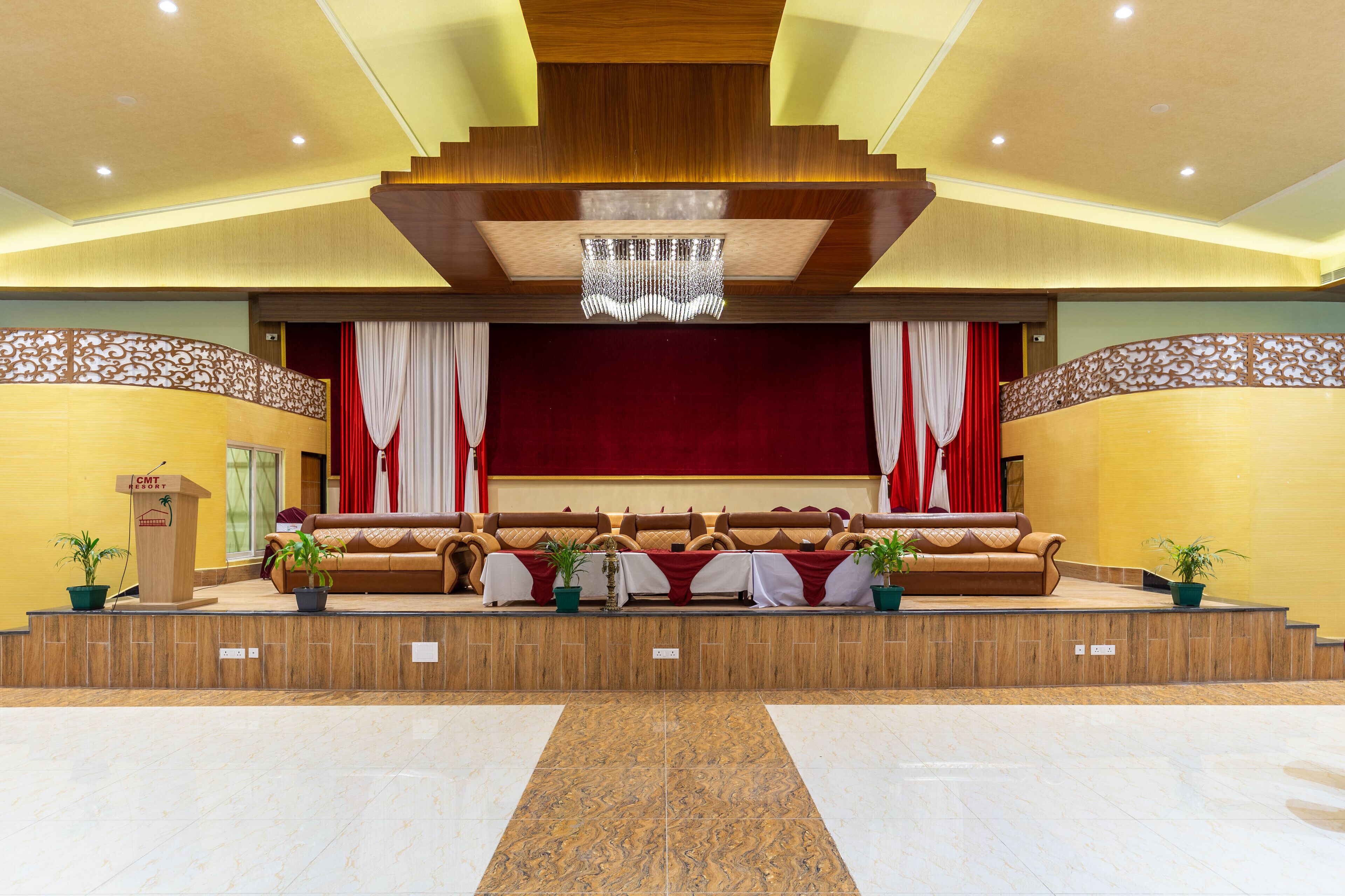 A lobby with a stage, sofas, potted plants, and a wooden podium.
