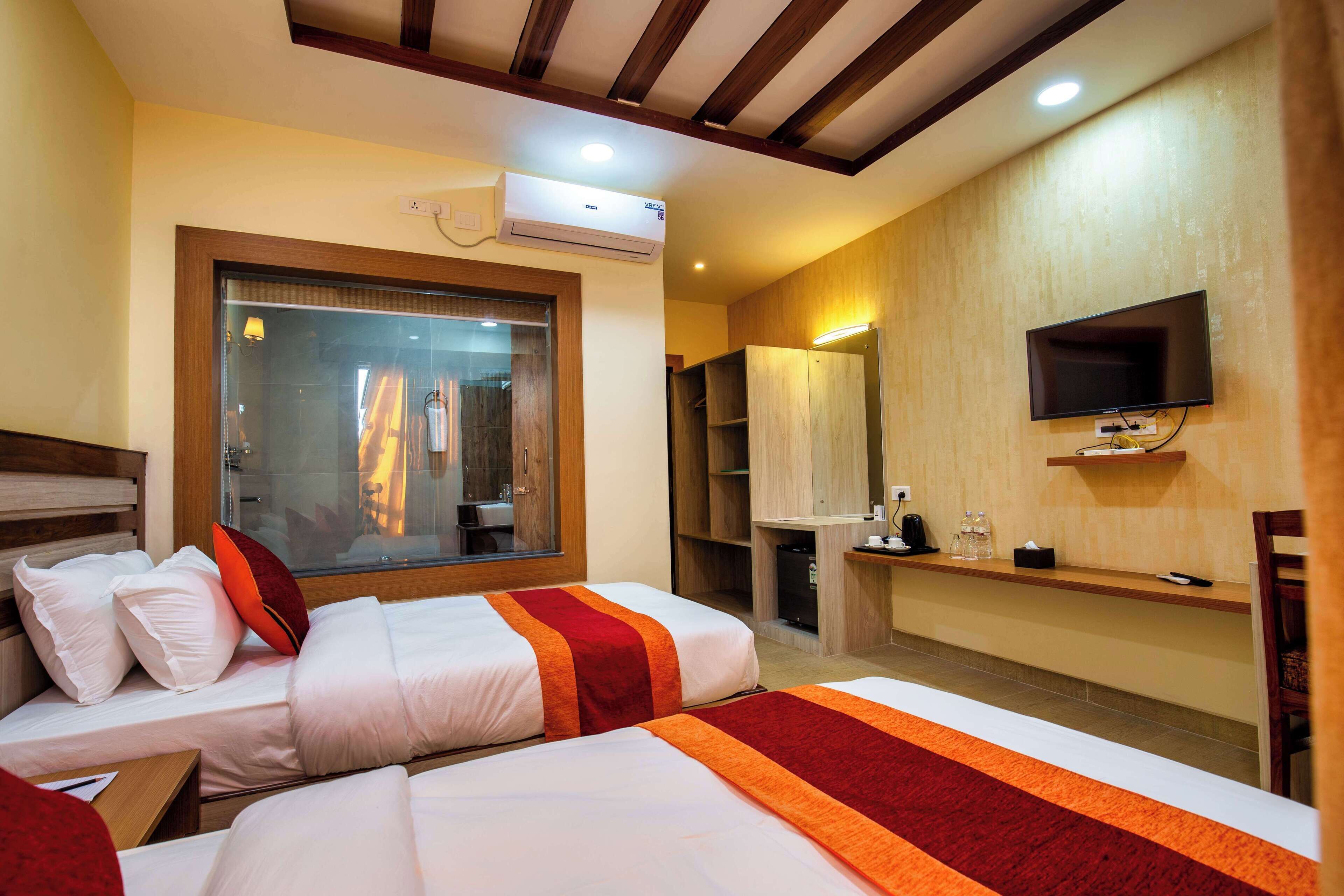 Een hotelkamer met twee bedden, een televisie, een airconditioner en een raam met uitzicht.