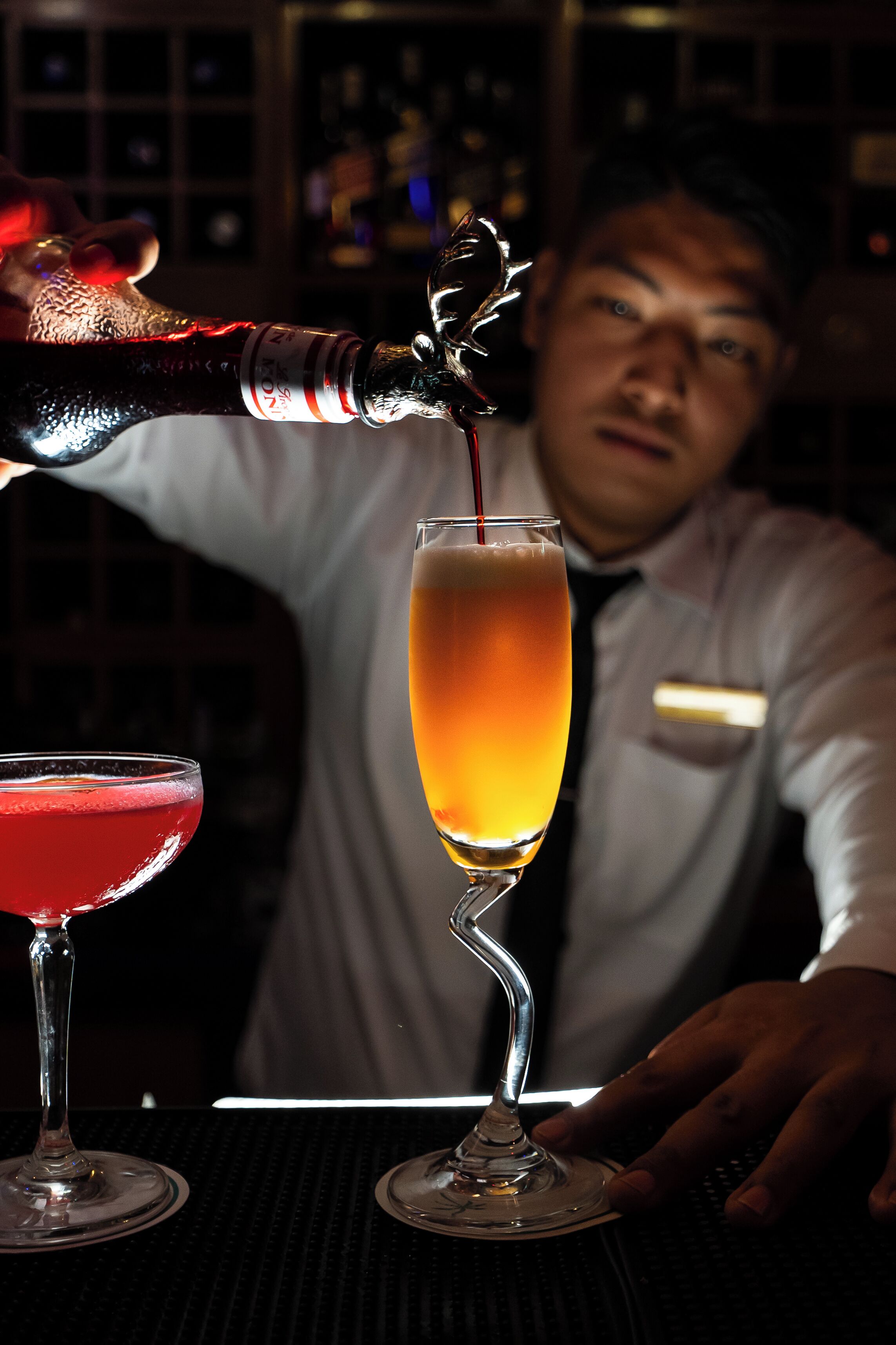 Een barman schenkt een drankje in een hoog glas.