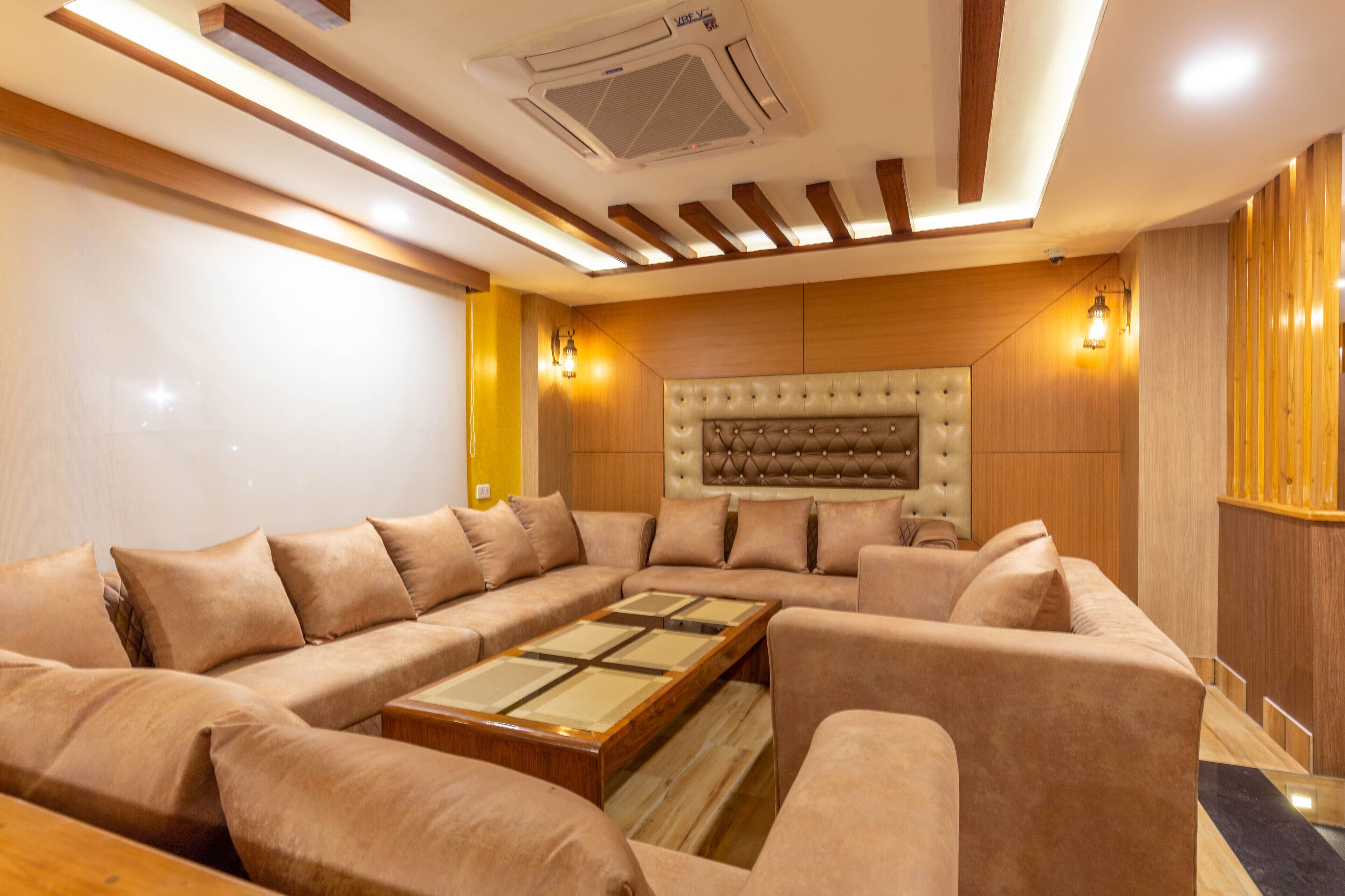 A modern living room with a sectional sofa, a tufted headboard, recessed lighting, and a wooden accent wall.