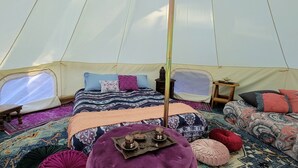 Uma tenda com cama, almofadas, uma mesinha e um tabuleiro decorativo.