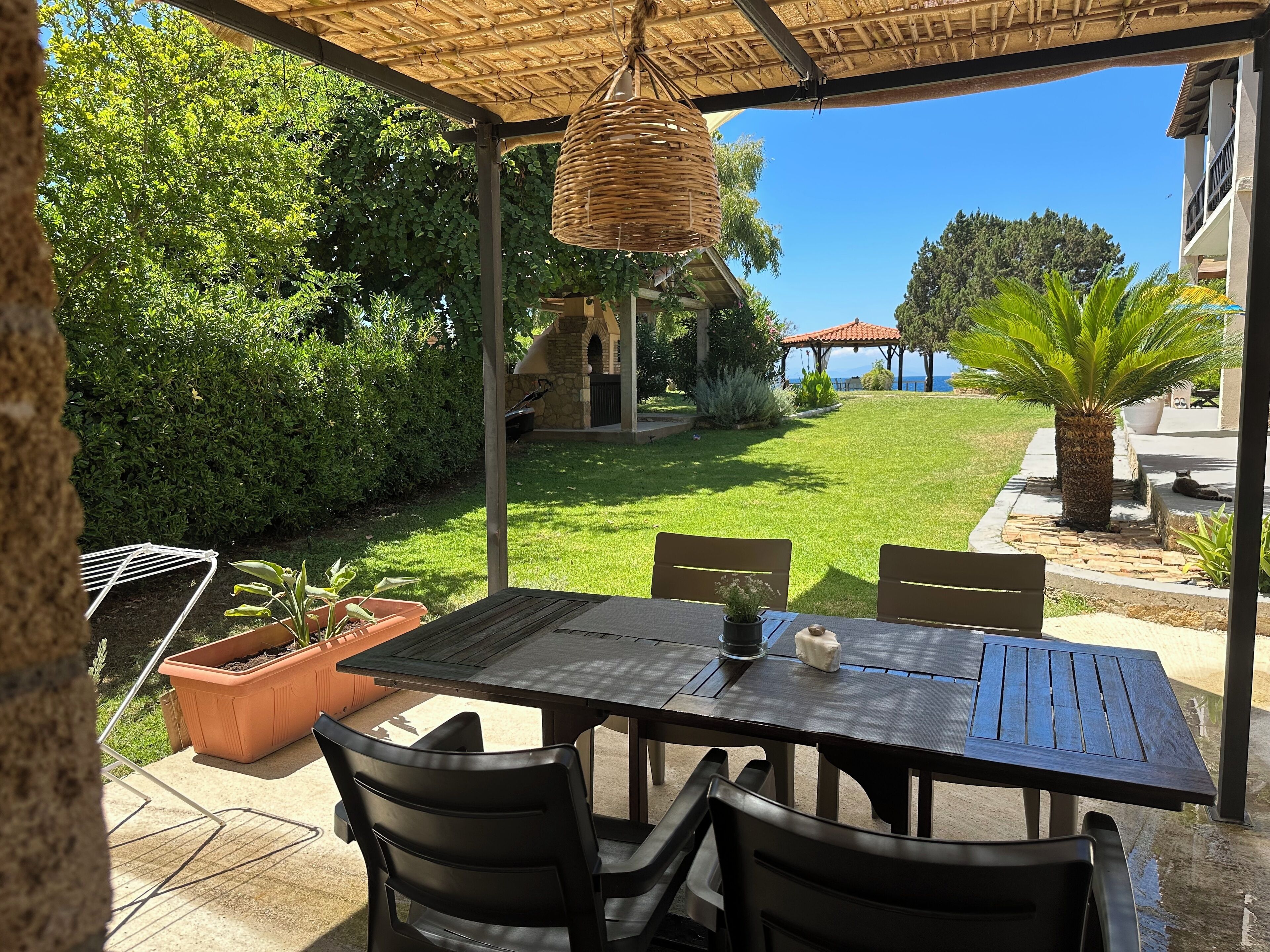 Un patio al aire libre con una mesa y sillas, rodeado de follaje y vistas al mar.