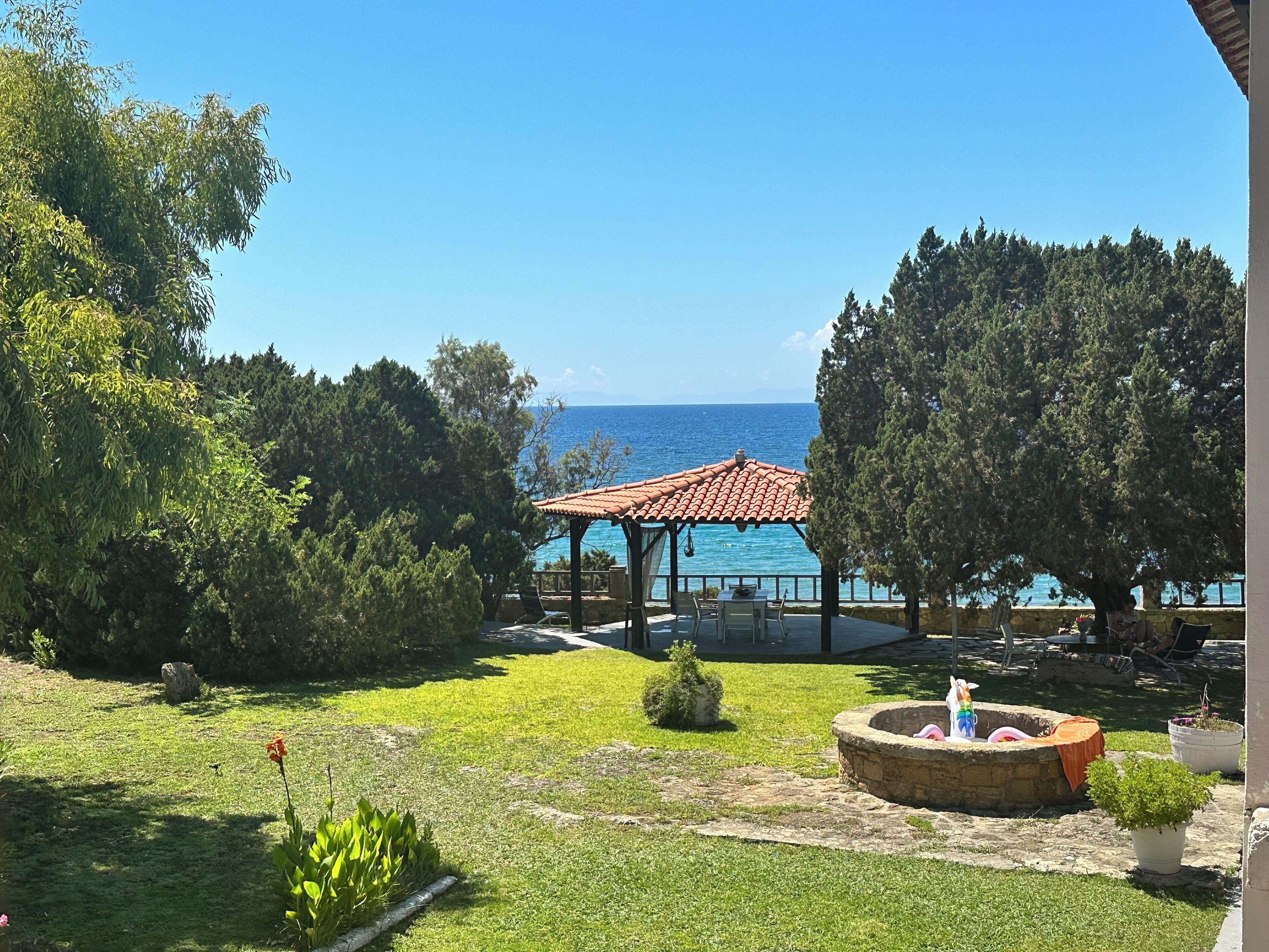 Ein Garten mit einem Gartenhaus, einem Stebrunnen und Blick auf das Meer.