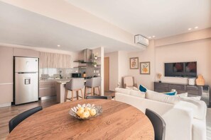 Una cocina moderna con comedor, una sala de estar con sofá y televisor, y una mesa de comedor con fruta.