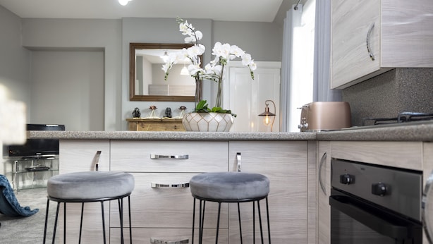 Une cuisine moderne avec deux tabourets de bar, un grand îlot central agrémenté d’un vase de fleurs blanches, une cuisinière et un four à micro-ondes.