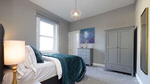 Une chambre à coucher comprenant un lit, une table de chevet, une lampe, une commode, une armoire et un tableau accroché au mur.